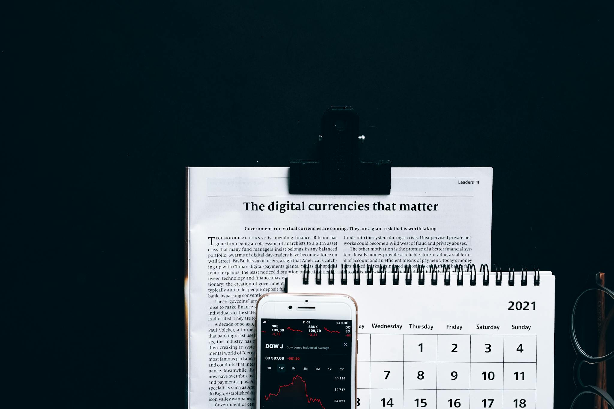 Digital currencies article with smartphone stock market app and calendar on black surface.